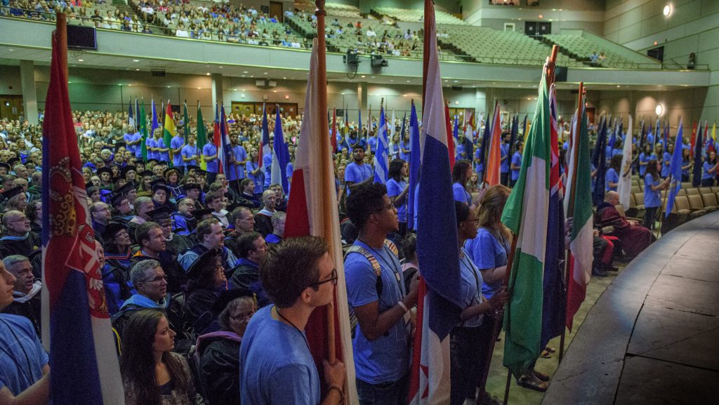 Students with flags and Faculty in regalia in auditorium.