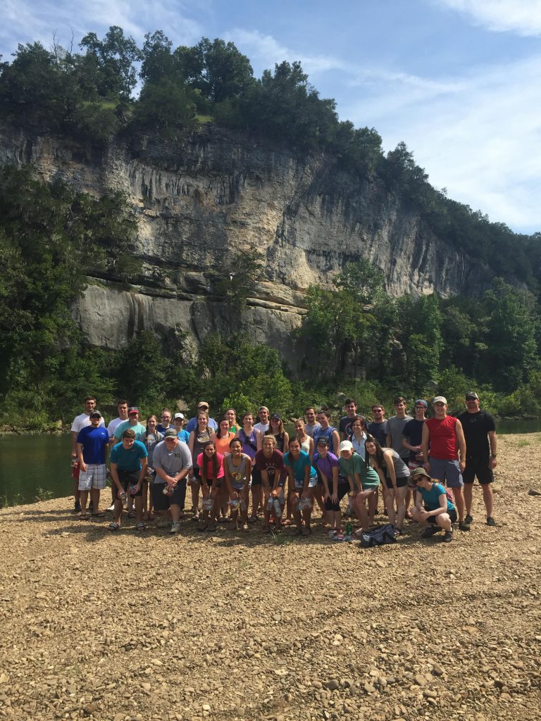 Students in front of cliff by a river.