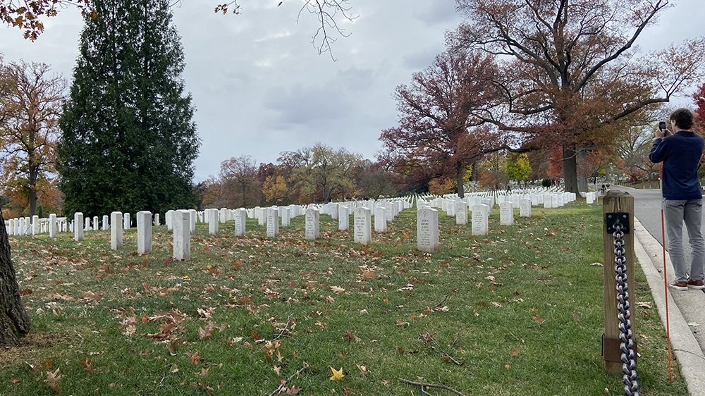 Student Max Thweatt stands to the right of the photo taking his own picture of a landscape of tombstones at Arlington National Cemetery in Washington, D.C.