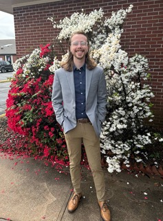 Kennedy Barden smiles in a suit in front of a flowering tree.