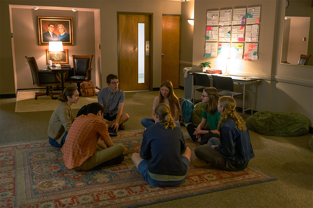 students sit on the floor in a low lit room to pray