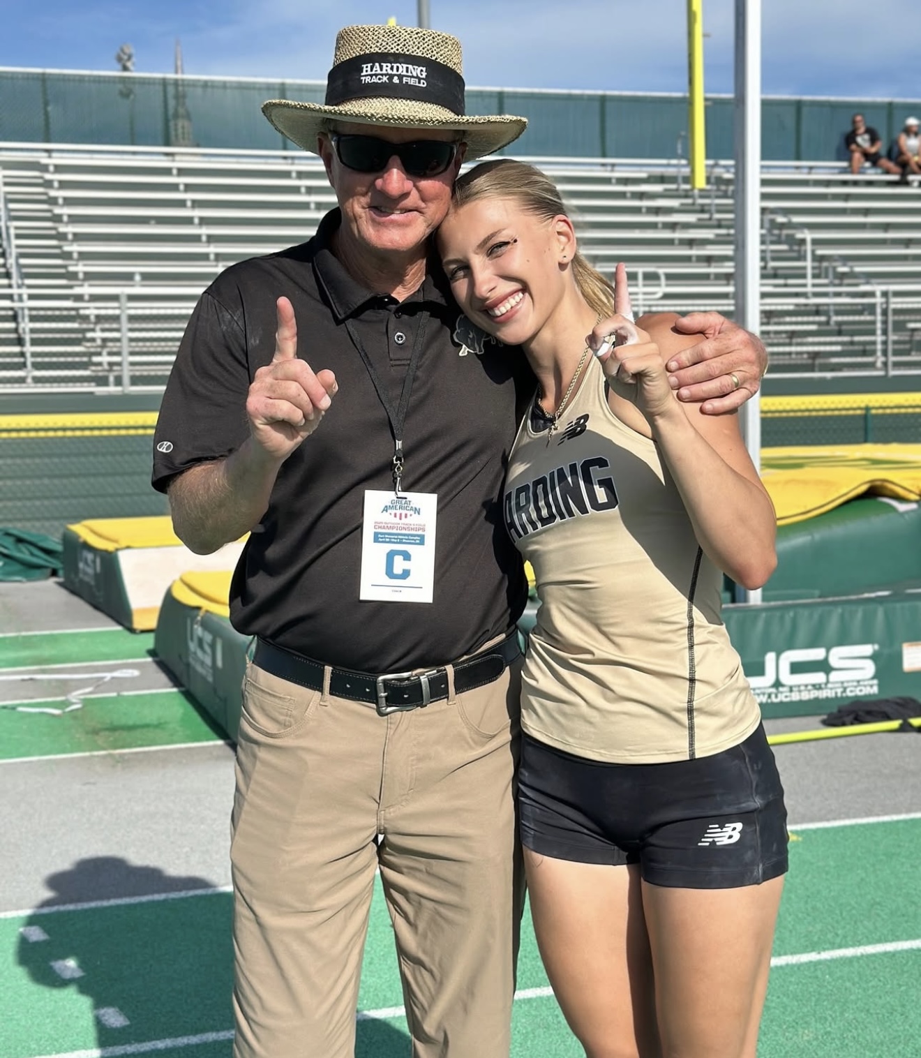 Coach Don Hood and Karyna Vehner embrace while holding up one finger to indicate first place at the GAC track and field champtionship