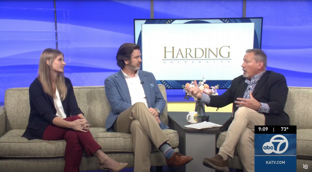 a white female speaking with two males in a news studio
