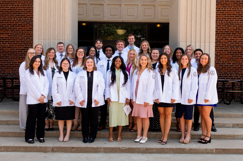 College of Pharmacy students stand smiling together in their white coats